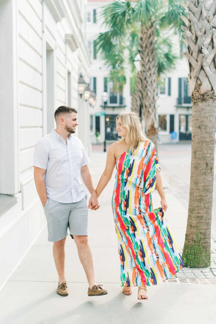 walking pose of couple under palm trees wearing vibrant one shoulder boho maxi dress
