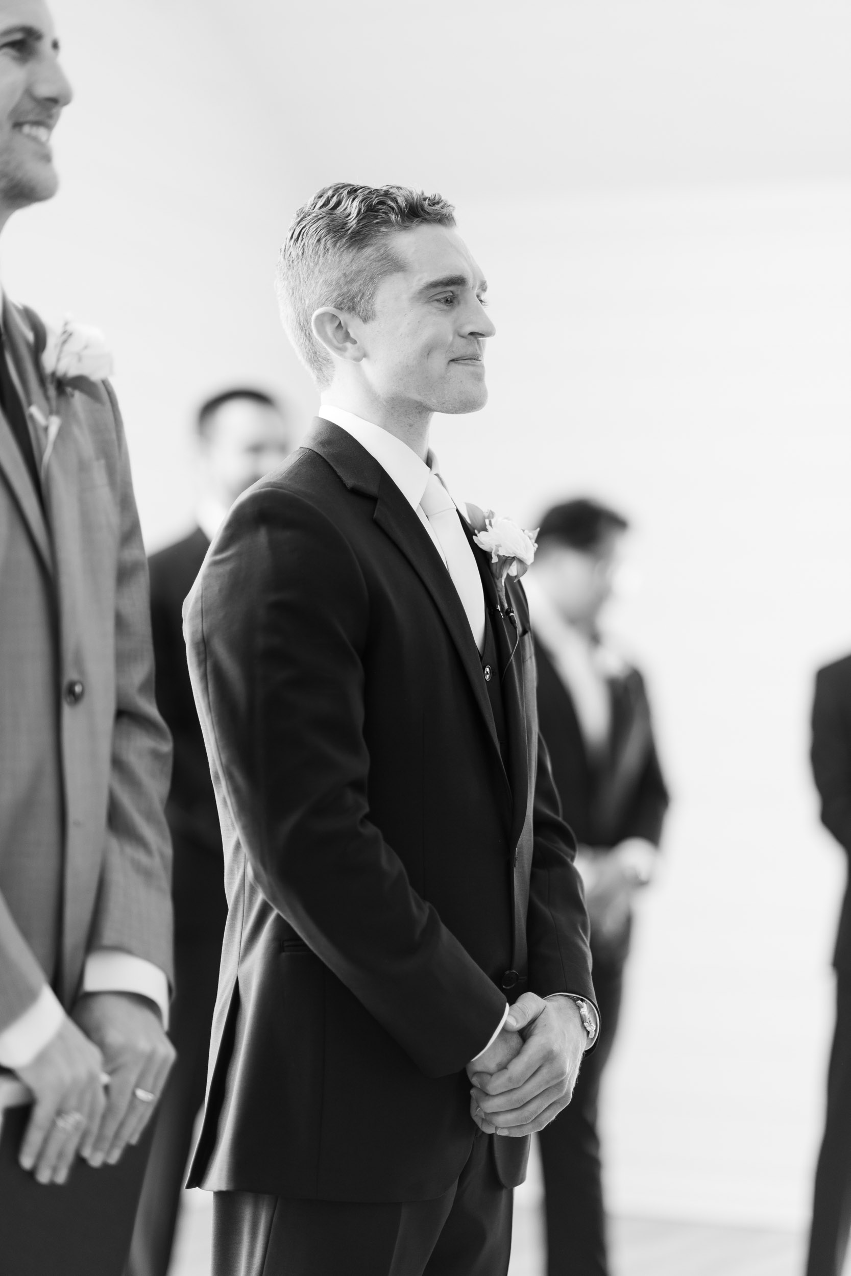 black and white portrait of the groom as the bride walks down the aisle