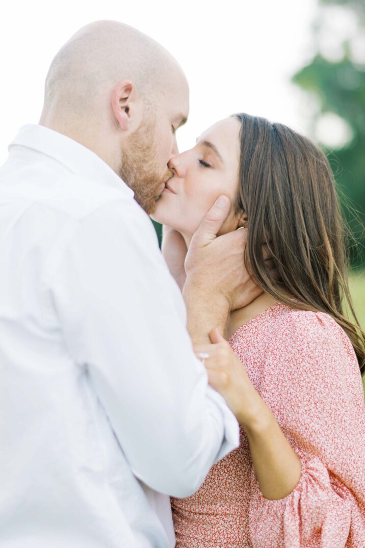 engagement session in a field with couple sharing a kiss