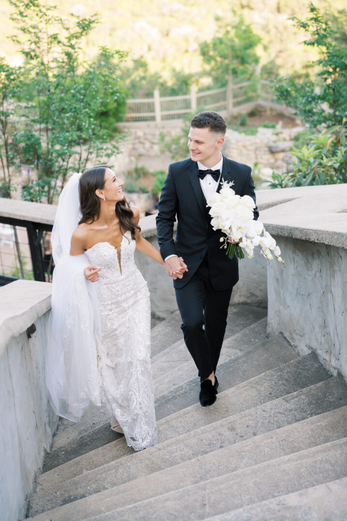 bride and groom holding hands walking up stairs white florals Italian inspired wedding travel 
